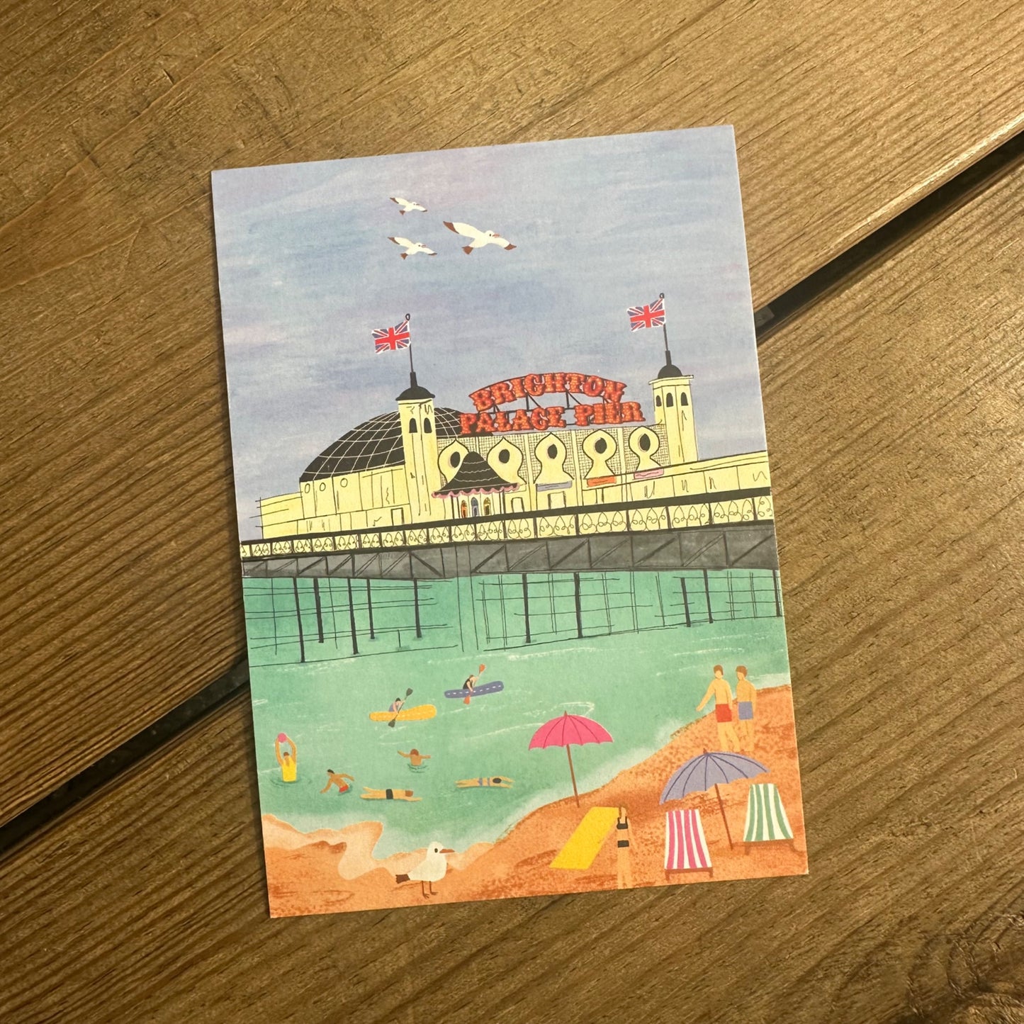 A postcard showing an illustration of Brighton Palace Pier, with people enjoying the beach in the foreground