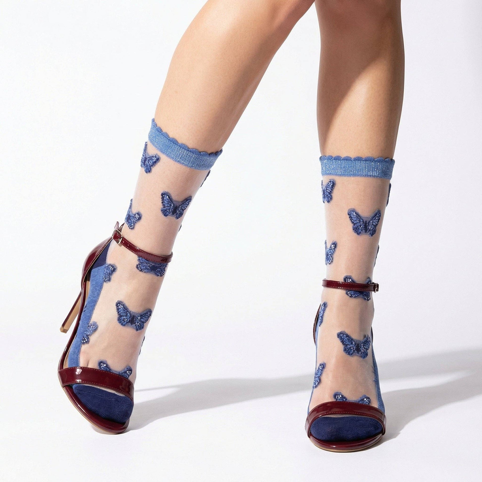 Sheer socks with blue butterfly pattern worn with high-heeled shoes on a white background
