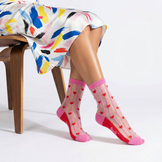 Person wearing pink socks with heart patterns sitting on a wooden chair.