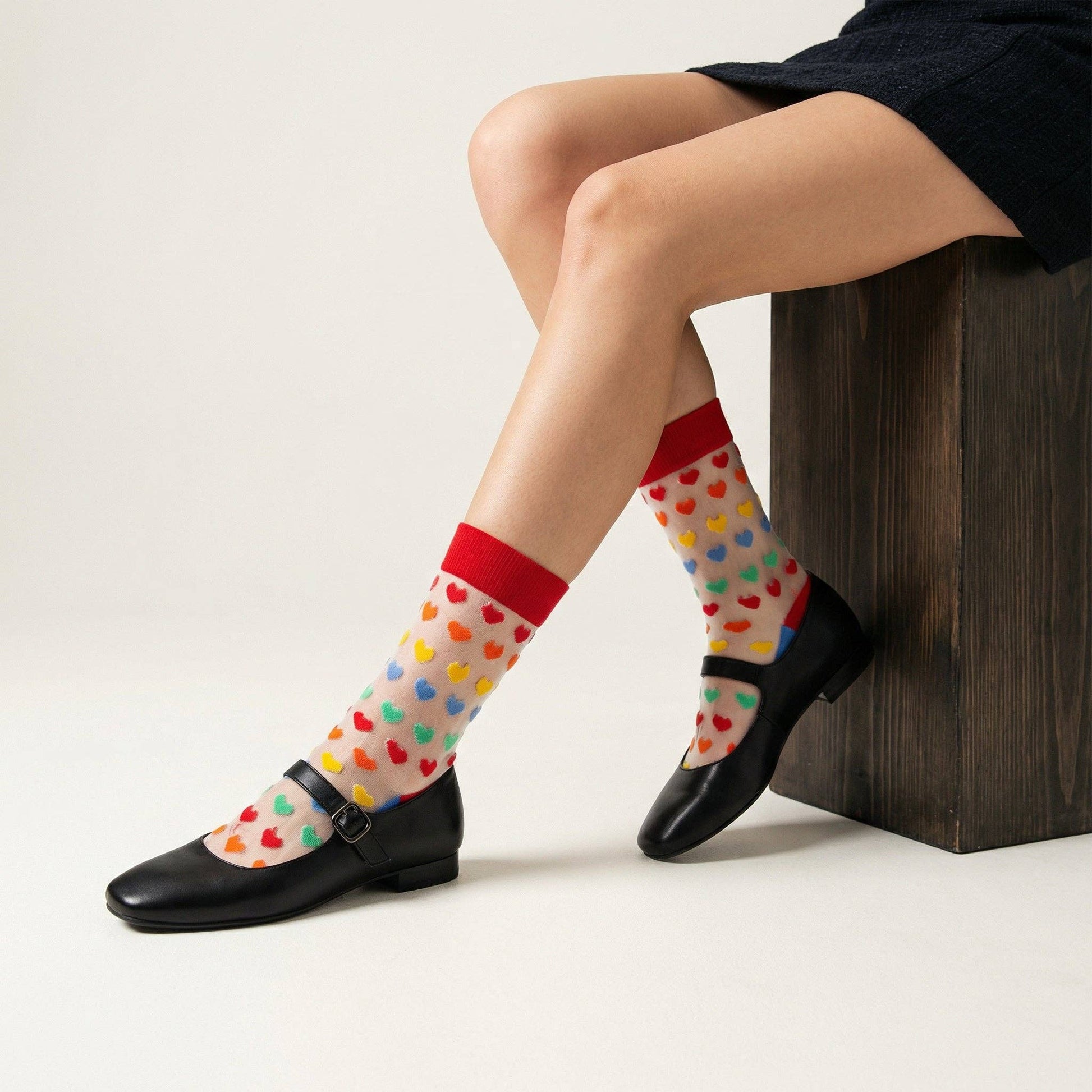 Person wearing colorful polka dot socks with love heart shapes. They sit on a wooden box, showing off the socks under black shoes.