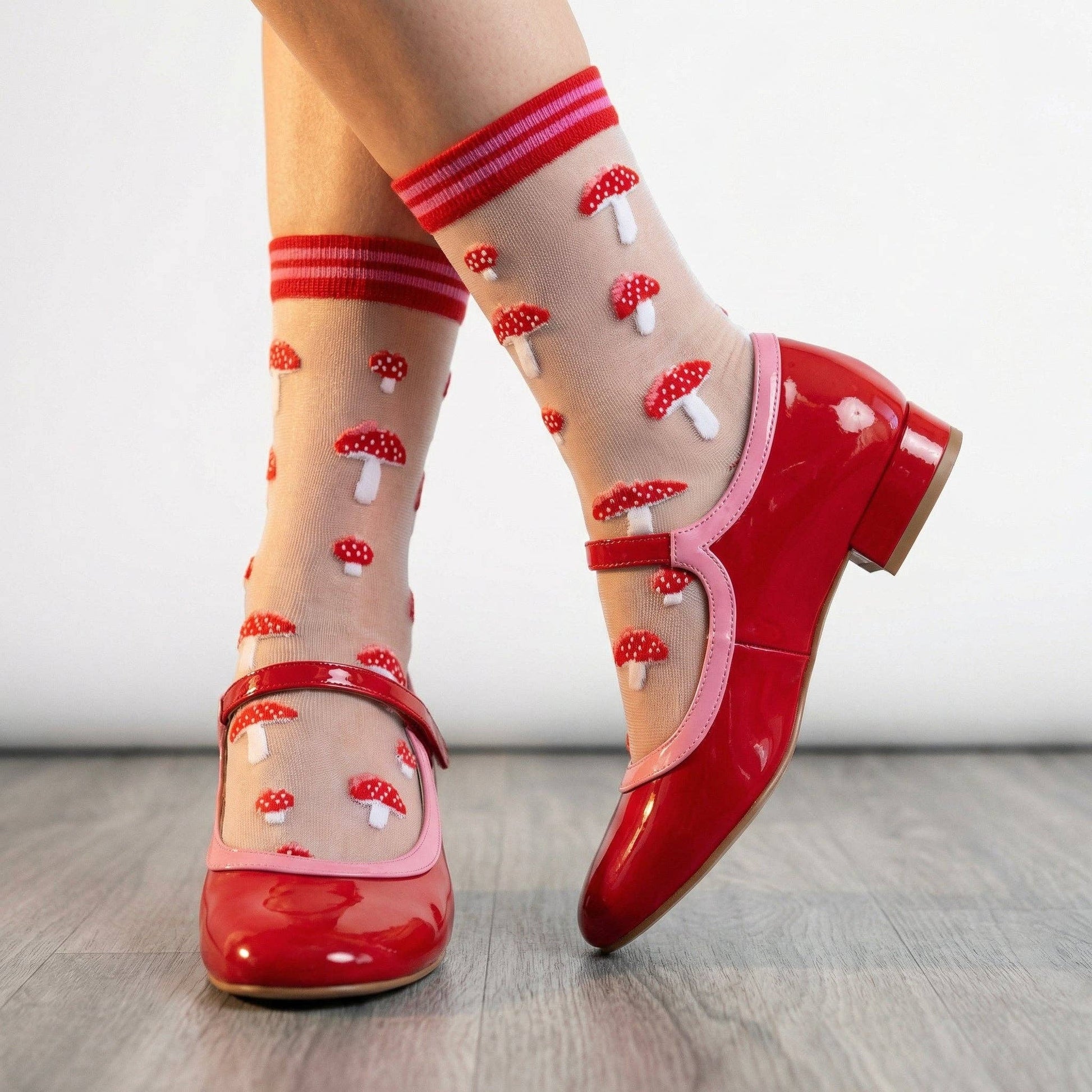 Red shoes with transparent socks featuring mushroom patterns on a light wooden floor.