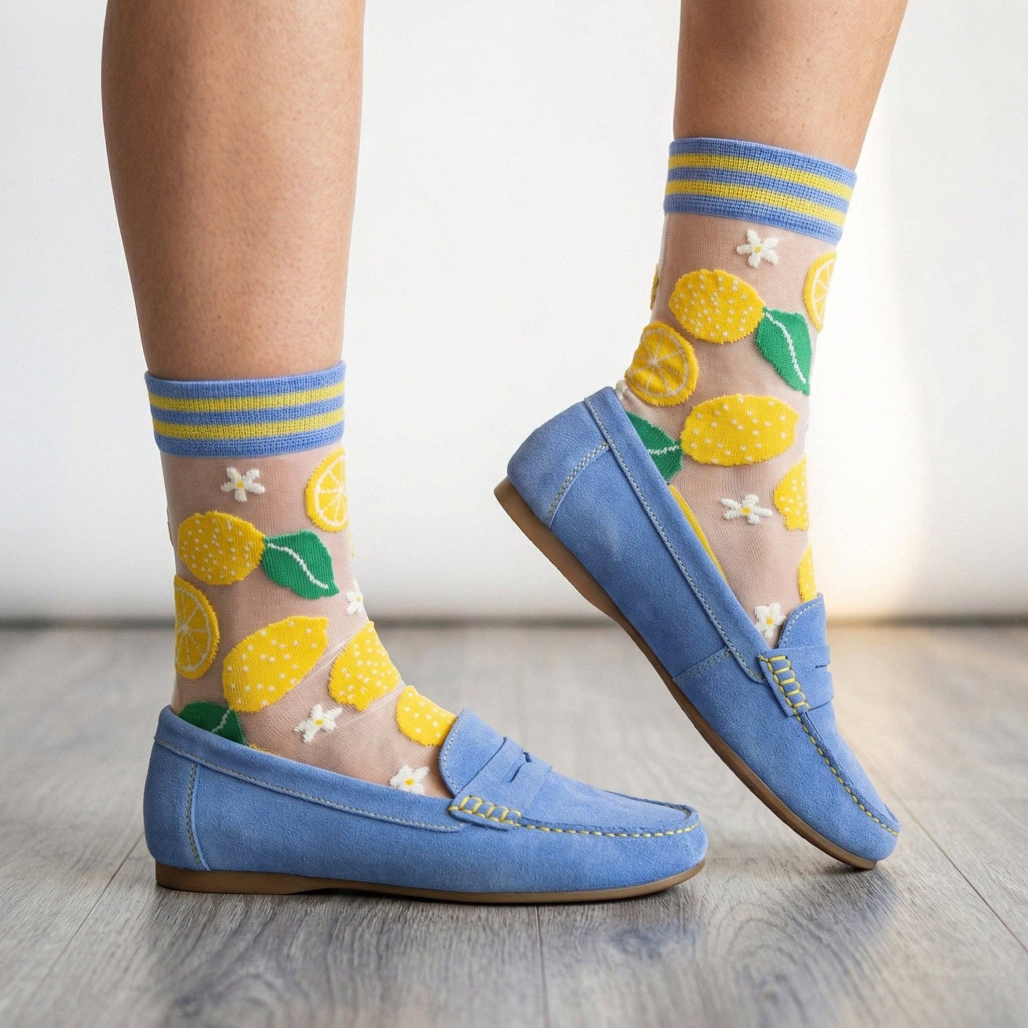Sheer socks with lemon design worn with blue loafers on a light wooden floor.