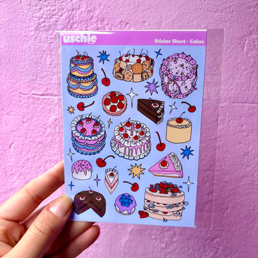 A hand holds a clear plastic sheet owith cute, colorful illustrated cakes, pastries, and cherries against a textured pink wall. The brand name 'usechie' is visible in the top left corner of the sticker sheet.