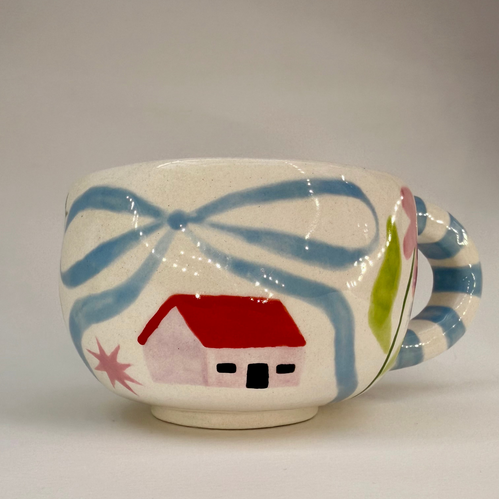 Ceramic cup with abstract design and small house illustration on a plain background