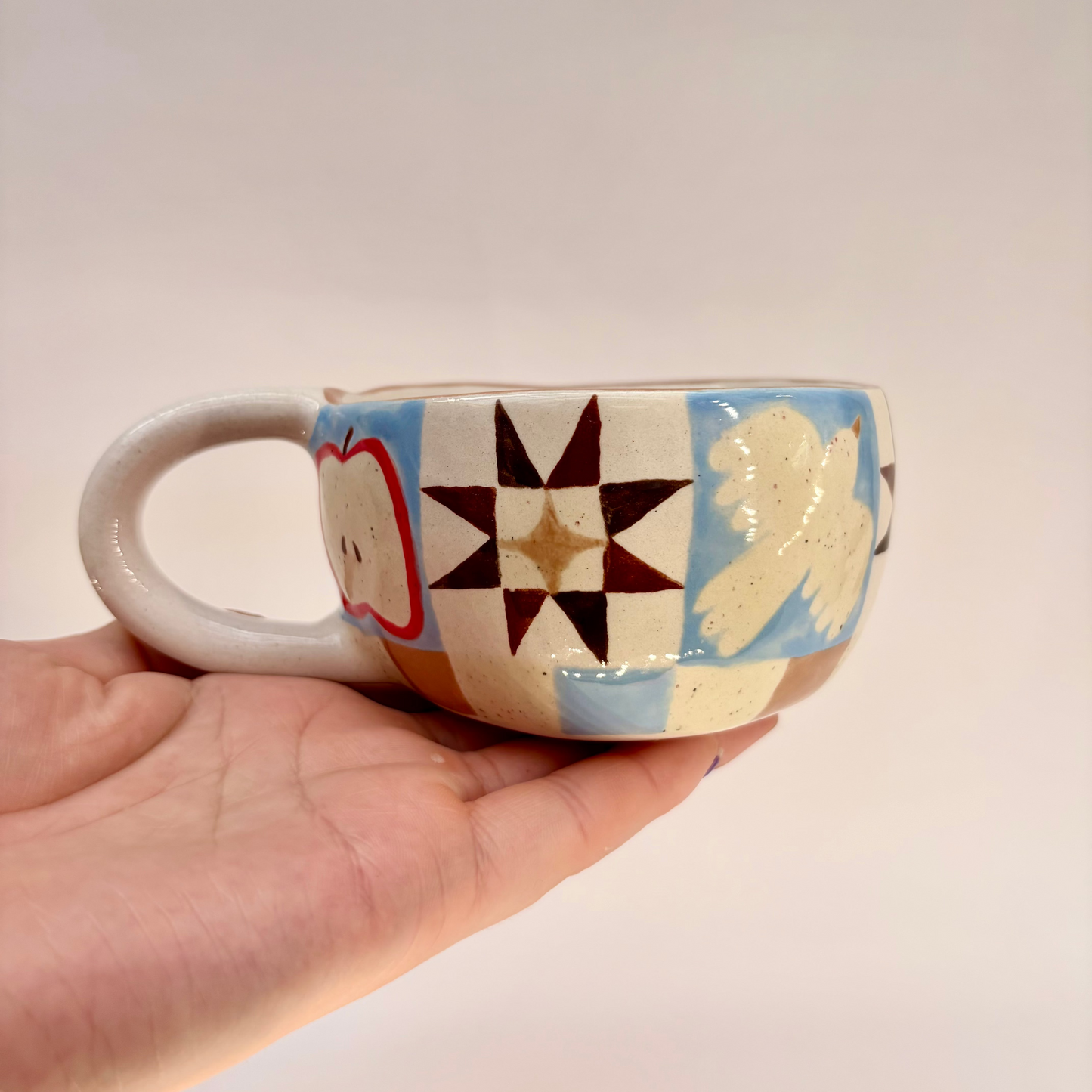 Hand holding a ceramic cup with colorful patterns on a plain background