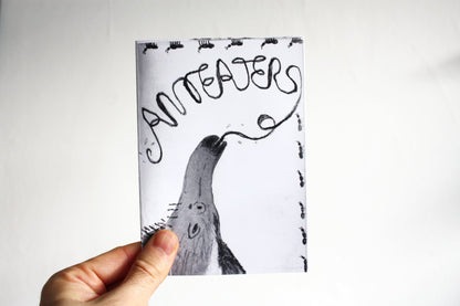Hand holding a zine with a drawing of an anteater against a white background