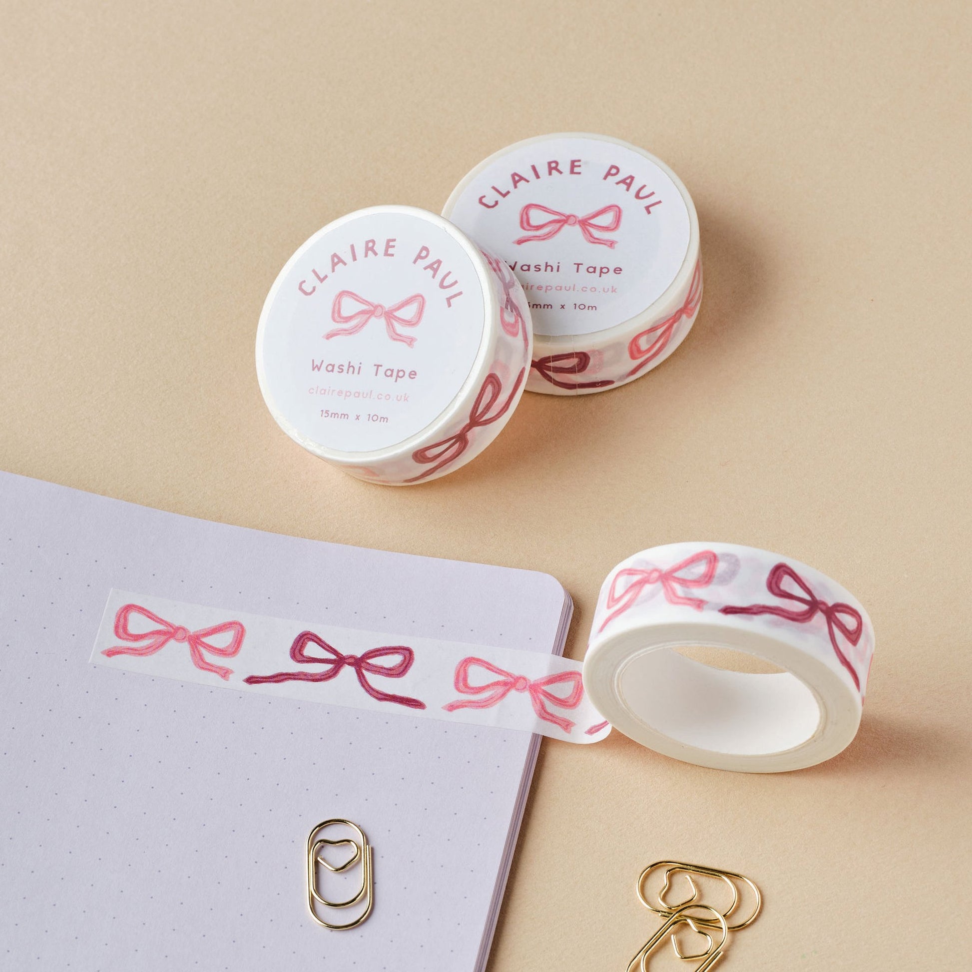 Two rolls of washi tape with pink bows set down on a beige background.