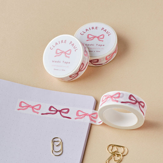 Two rolls of washi tape with pink bows set down on a beige background.