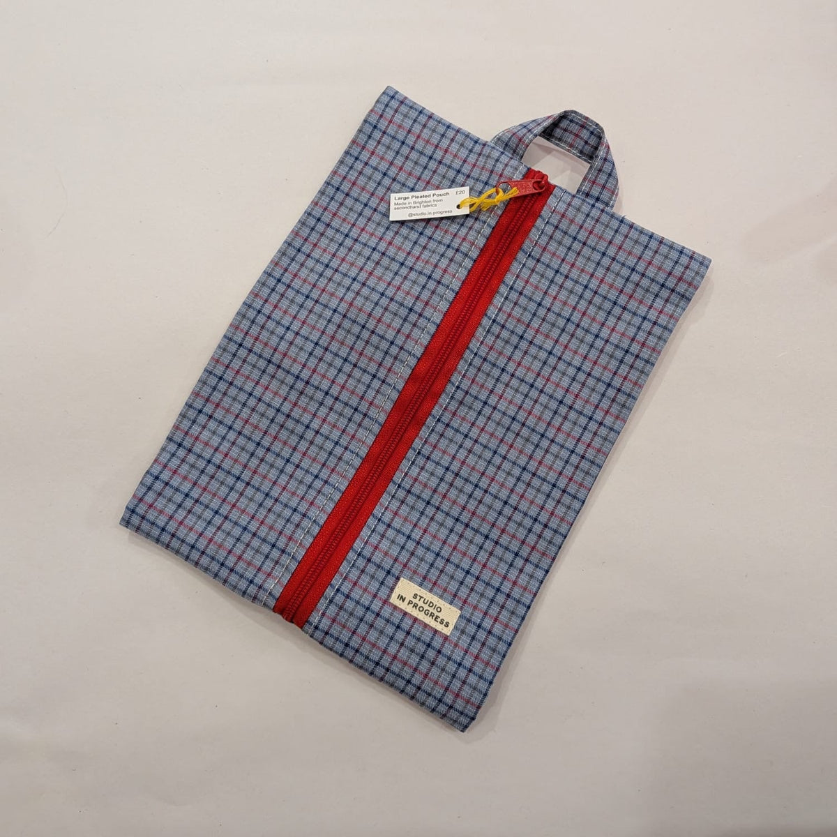 A folded plaid shirt in blue, red, and white with a prominent red zipper running down the center, shown on a light gray background.