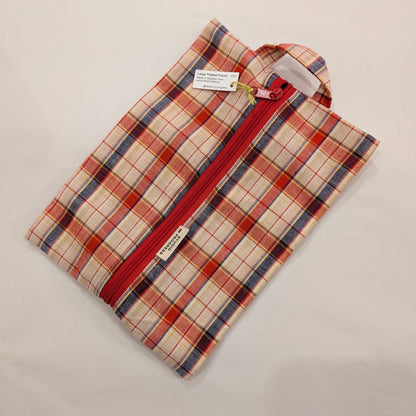 A small zippered pouch with a red and cream plaid pattern, featuring a red zipper, a fabric loop handle, and two small white tags, shown on a light beige background.