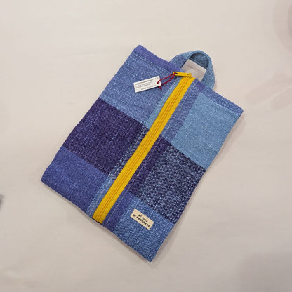 A zippered fabric pouch or small bag made from patchwork blue and purple woven material, with a bright yellow zipper and a small sewn label, photographed on a plain light background.