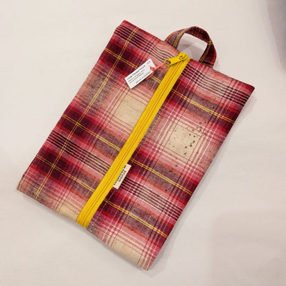 A fabric zippered pouch with a red, pink, and beige plaid pattern, featuring a bright yellow zipper and a matching yellow top handle, shown on a plain light background.