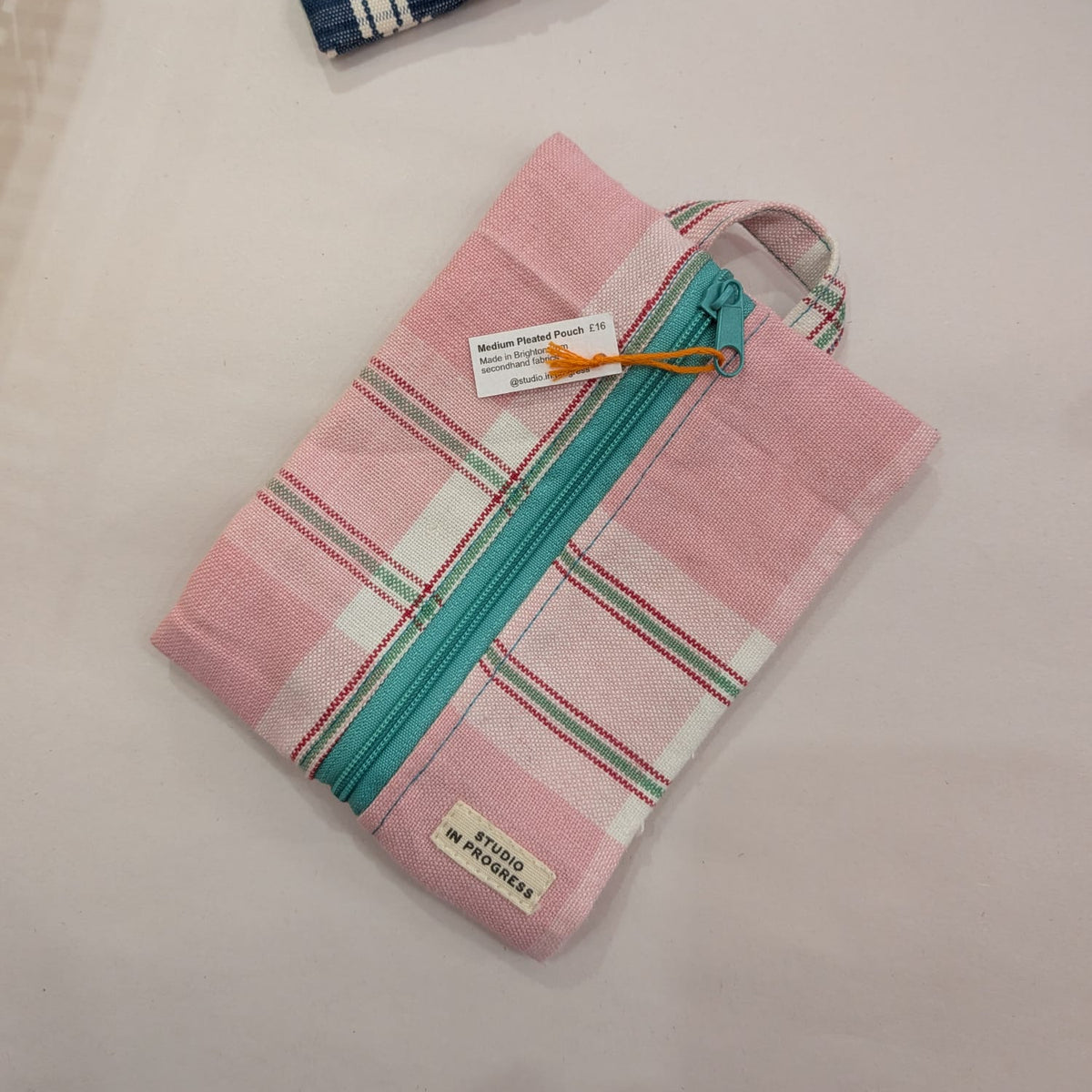A pink woven zippered pouch with a teal zipper and striped details, shown on a light surface next to another blue and pink striped pouch.