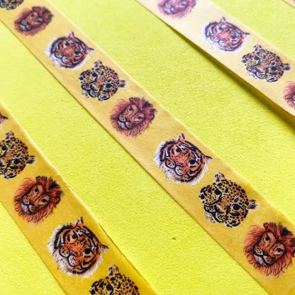 Yellow wash tape featuring repeated big cat face prints including tiger, leopard, and lion heads, laid diagonally against a bright yellow background.