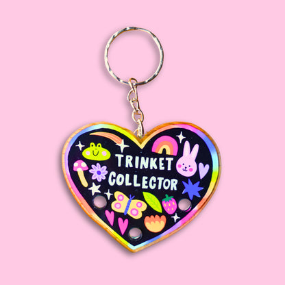 Heart-shaped keychain with 'Trinket Collector' text and colorful designs on a pink background